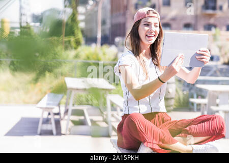 Giovane donna seduta sul tavolo in un giardino della birra utilizzando tablet Foto Stock