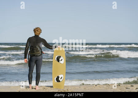 Vista posteriore del kiteboarder in piedi con la sua tavola da surf in spiaggia Foto Stock