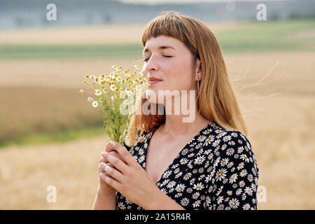 Sorridente giovane donna con gli occhi chiusi maleodoranti mazzetto di fiori di camomilla in natura Foto Stock