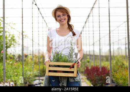 Ritratto di giovane e bella donna che mantiene una scatola di legno con piante in serra Foto Stock