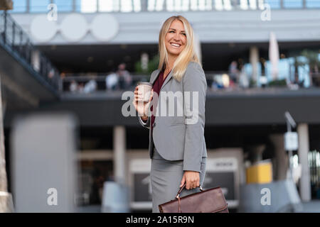 Ritratto di felice bionda imprenditrice con caffè di andare e valigetta Foto Stock