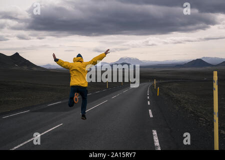 Uomo felice salti di gioia su una strada vuota, Islanda Foto Stock