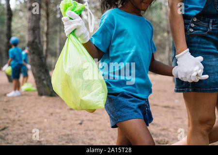 Donna e ragazza camminare mano nella mano raccogliere rifiuti in un parco Foto Stock