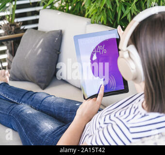 Giovane donna con la compressa uncon smart home le funzioni di comando e le cuffie Foto Stock