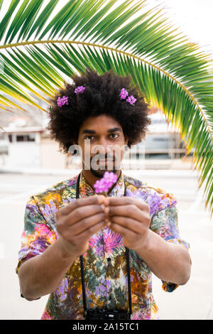 Ritratto di uomo con fiori nei capelli indossare magliette colorate Foto Stock
