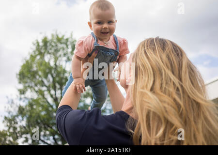 Felice madre sollevamento bambina all'aperto Foto Stock