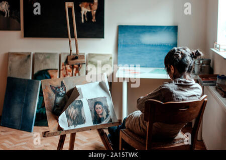 Vista posteriore di una donna artista seduto nel suo studio di fronte a un dipinto Foto Stock