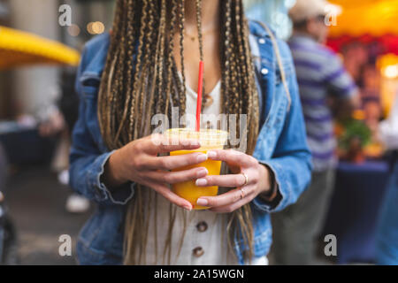 Donna di mani tenendo una tazza di plastica di succo d'arancia fresco Foto Stock