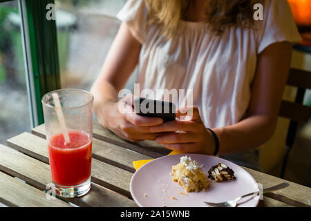 Close-up di giovane donna seduta a tavola con un smoothie tramite telefono cellulare Foto Stock