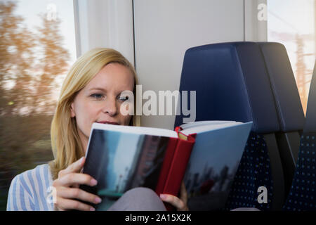 Donna seduta in un treno, la lettura di un libro Foto Stock