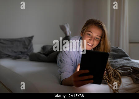 Felice giovane donna giaceva a letto a casa di notte utilizzando tablet Foto Stock