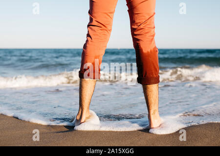 Vista posteriore dell'Uomo con pantaloni arancione in piedi su una spiaggia a bordo d'acqua Foto Stock