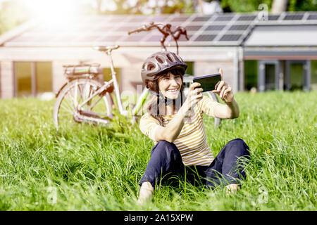 Felice donna seduta su un prato con bicicletta prendendo un selfie Foto Stock