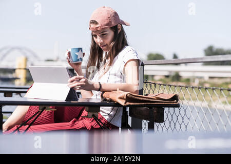 Giovane donna rilassante in un giardino della birra utilizzando tablet Foto Stock