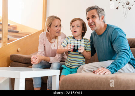 Genitori felici con il figlio la riproduzione di video gioco sul lettino a casa Foto Stock