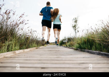 Vista posteriore della coppia giovane jogging sulla passerella in legno Foto Stock