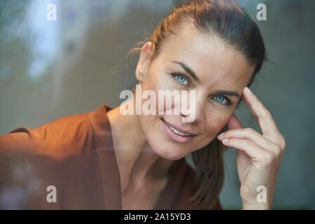 Ritratto di sorridere donna attraente dietro il vetro di finestra Foto Stock