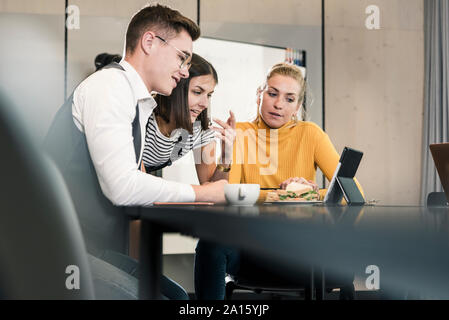 I colleghi avente una riunione nella sala conferenze condivisione tablet Foto Stock