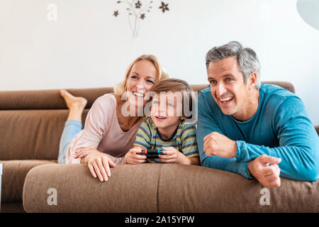 Genitori felici con il figlio la riproduzione di video gioco sul lettino a casa Foto Stock