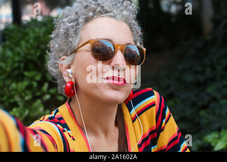 Ritratto di trafitto donna matura indossando occhiali da sole e auricolari Foto Stock