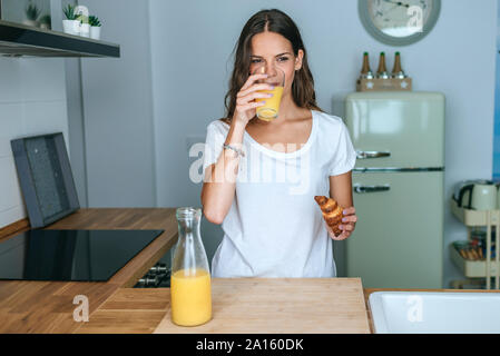 Giovane donna avente la colazione con succo di frutta e croissant in cucina Foto Stock
