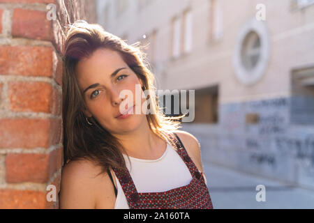 Giovane donna appoggiata sul muro di mattoni e guardando la fotocamera Foto Stock