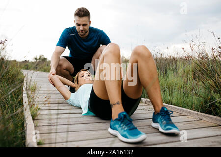 Pareggiatore femmina di formazione con il suo allenatore su una passerella in legno, sit-up Foto Stock