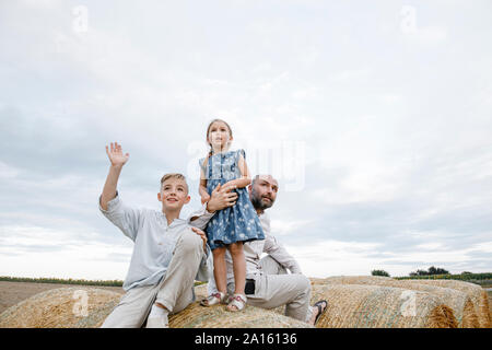 Padre e i suoi bambini seduti su balle di fieno, guardando il cielo Foto Stock