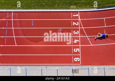 Vista aerea di una giovane atleta femminile giacente su un tartan via dopo aver attraversato la linea di finitura Foto Stock