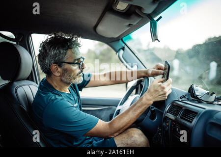 Uomo maturo seduta seduta nel suo veicolo fuoristrada controllare il suo smartphone Foto Stock