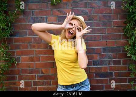 Ritratto di giocoso giovane donna in piedi in corrispondenza di un muro di mattoni Foto Stock