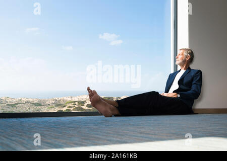 Imprenditore Senior seduto alla finestra panoramica che guarda fuori Foto Stock