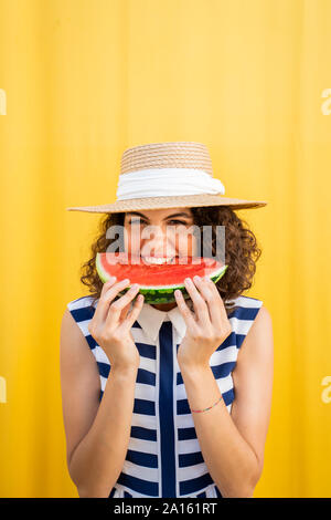 Ritratto di donna mangiare anguria, sfondo giallo Foto Stock