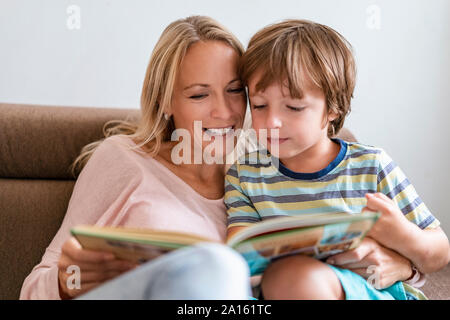 Madre e Figlio la lettura di un libro insieme sul lettino a casa Foto Stock