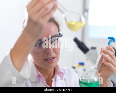 Scienziato esaminando una formula chimica in un pallone da laboratorio Foto Stock