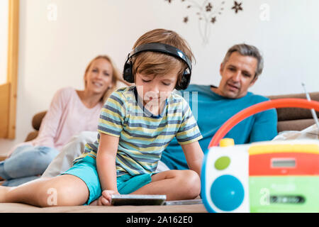 La famiglia sul divano di casa con ragazzo ascoltare musica con le cuffie Foto Stock