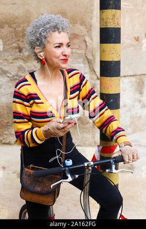 Ritratto di trafitto donna matura con bicicletta ascoltando musica con earphobnes e telefono cellulare Foto Stock