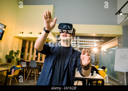 Giovane uomo asiatico in abiti casual indossando testa-montata la realtà virtuale gli occhiali. Uomo con occhiali vr in posa di studio moderno coworking Foto Stock