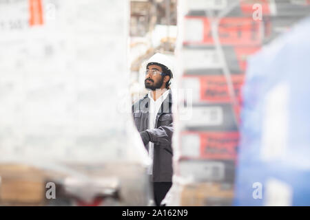 Giovane uomo indossare elmetto lavorando in un magazzino Foto Stock