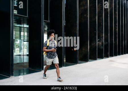 Uomo con zaino giallo, smartphone cuffie e camminare per la strada, Barcellona, Spagna Foto Stock