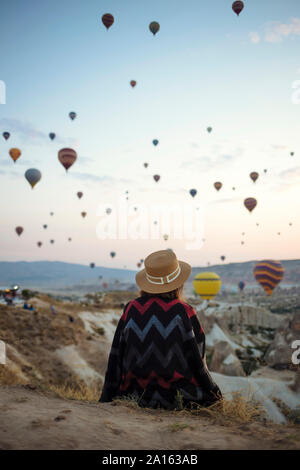 Giovane donna e i palloni ad aria calda di sera, Goreme, Cappadocia, Turchia Foto Stock