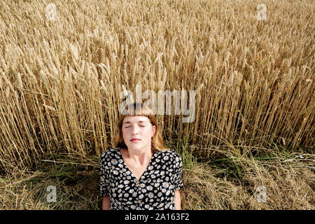 Ritratto di giovane donna con gli occhi chiusi rilassante nella parte anteriore del campo di grano Foto Stock