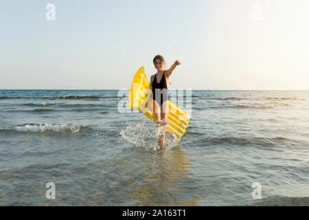Giovane donna con giallo airbed in spiaggia Foto Stock