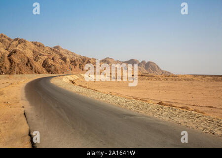 Strada vuota dalla formazione di roccia nel deserto contro il cielo blu chiaro Foto Stock