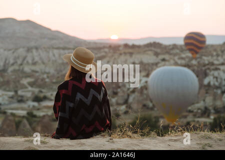 Giovane donna e i palloni ad aria calda di sera, Goreme, Cappadocia, Turchia Foto Stock