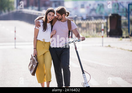 Coppia giovane con lo scooter elettrico a camminare sulla strada Foto Stock