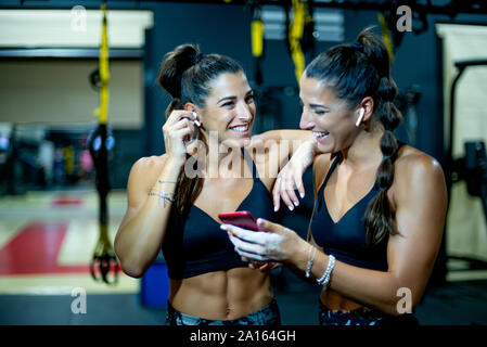 Twin felice sorelle in palestra con lo smartphone e le cuffie Foto Stock