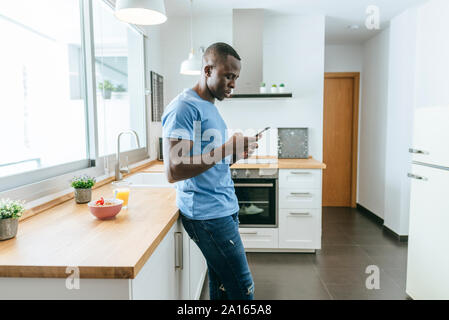 Giovane uomo utilizzando il cellulare in cucina a casa Foto Stock