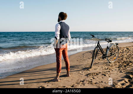 Ben vestito uomo con la sua bicicletta in piedi su una spiaggia Foto Stock