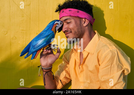 Giovane uomo nero in posa con un pappagallo di fronte ad una parete di colore giallo Foto Stock
